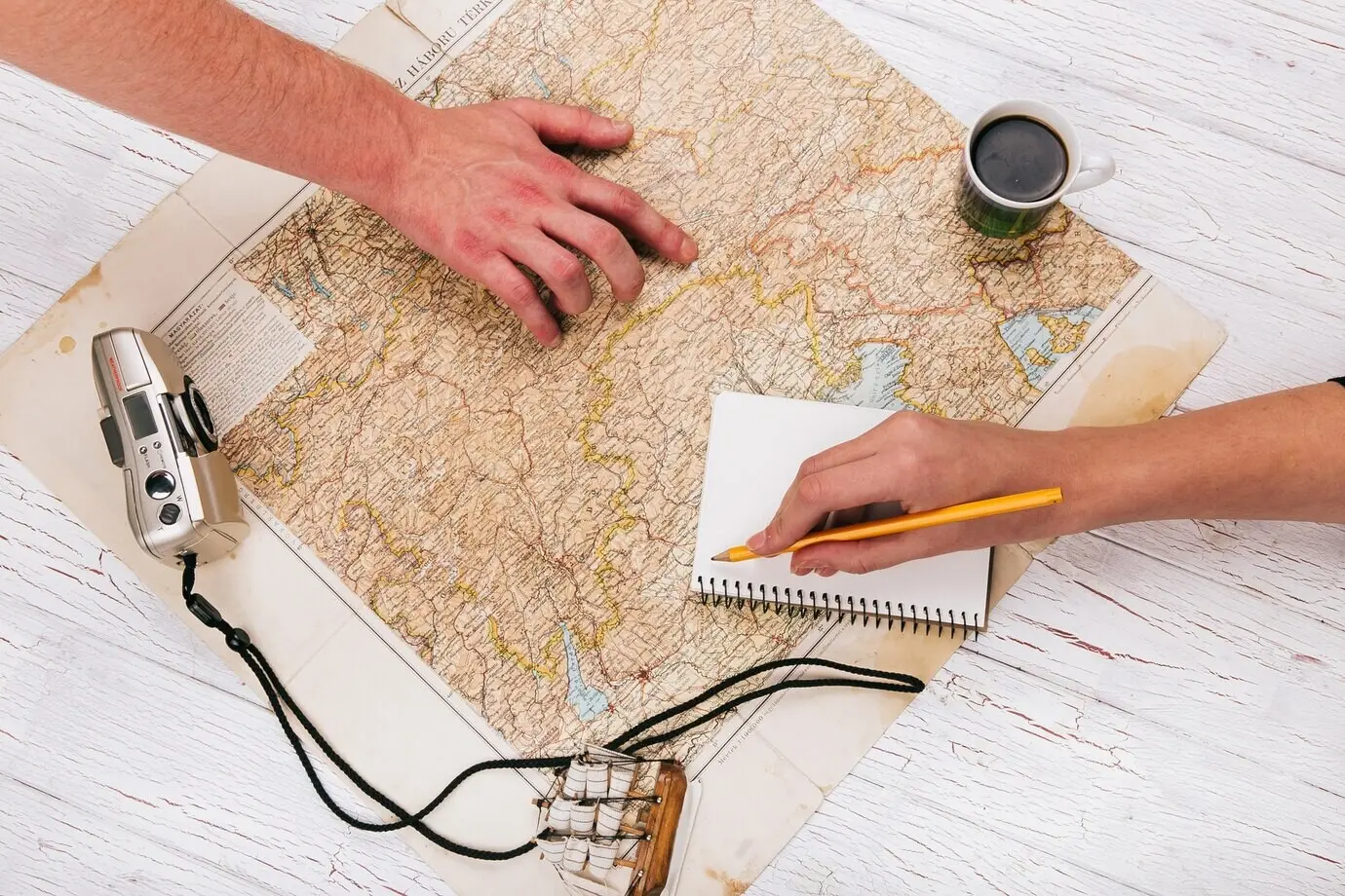 Männer halten ihre Hände auf einer Karte, mit Kaffee, Kamera und Notizbuch.